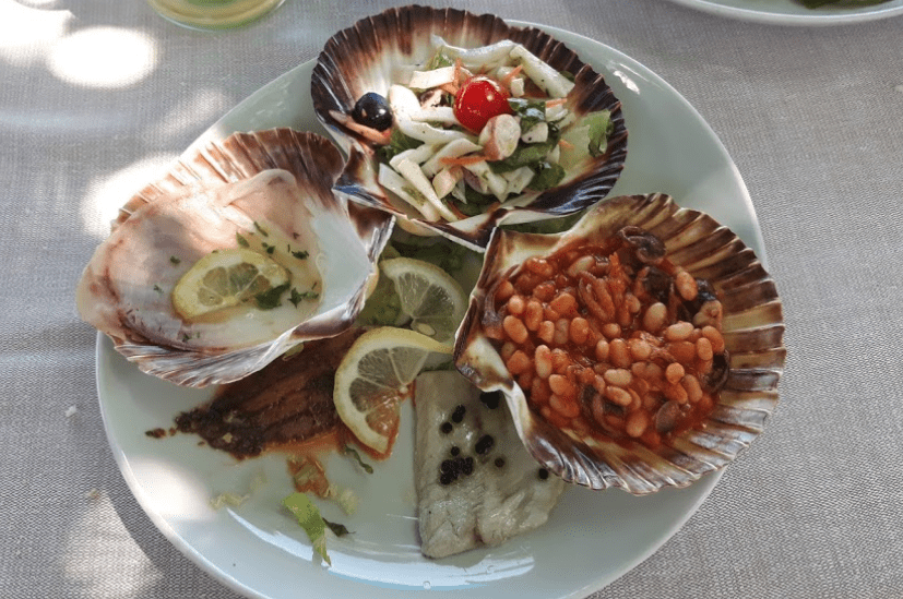 Quattro conchiglie con antipasti vari su un piatto.
