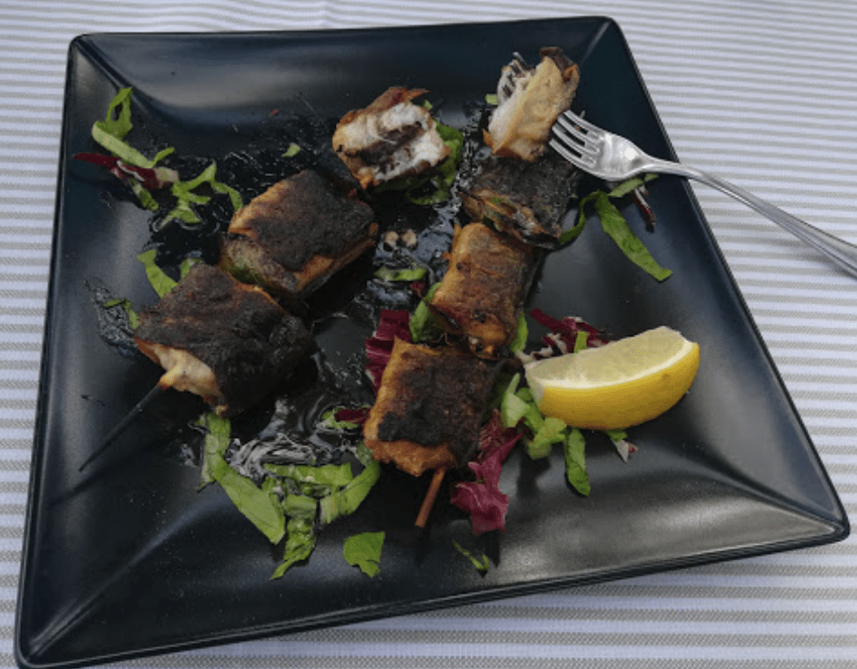 Spiedini di pesce su piatto nero con limone.
