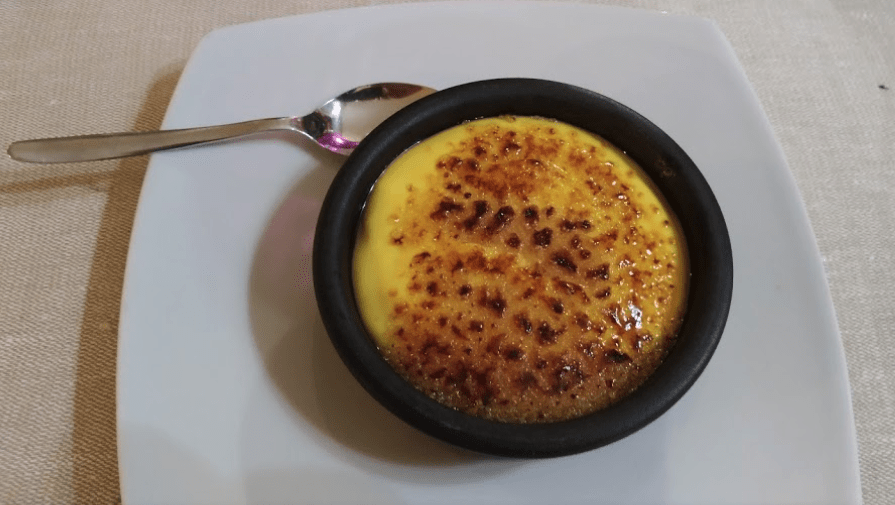 Crema catalana in ciotola nera su piatto bianco.