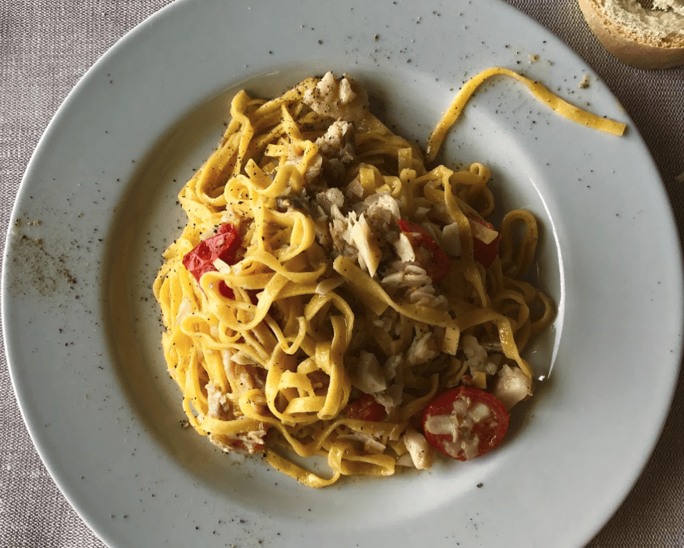 Tagliatelle con pomodorini e pesce su piatto bianco.