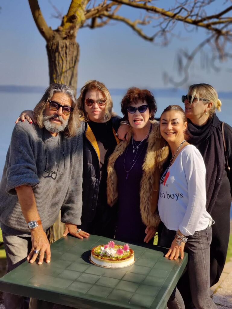 Cinque persone sorridenti attorno a un tavolo con torta.
