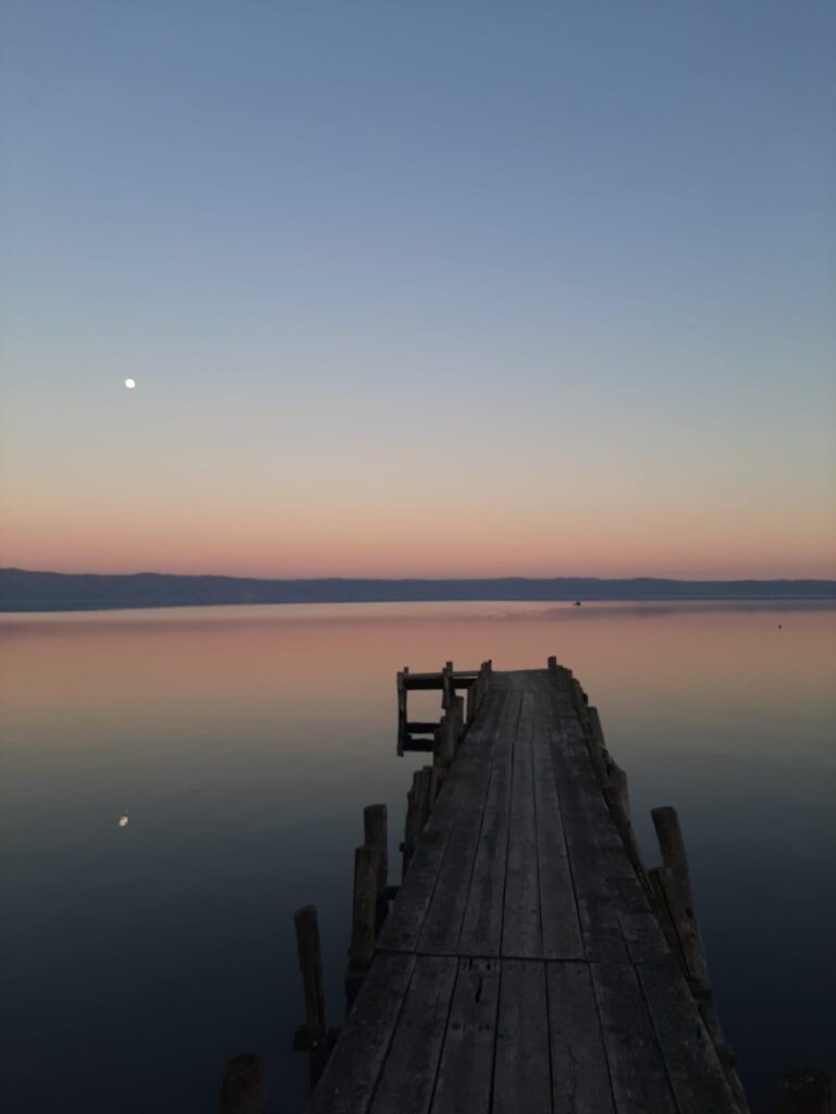 Molo di legno al tramonto su lago calmo.