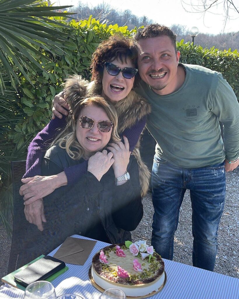 Tre persone sorridenti con torta su tavolo all'aperto.