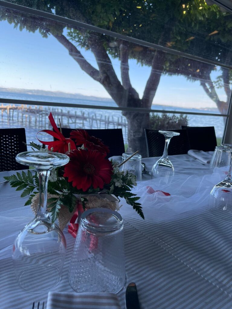 Tavola apparecchiata con fiori rossi, vista mare.