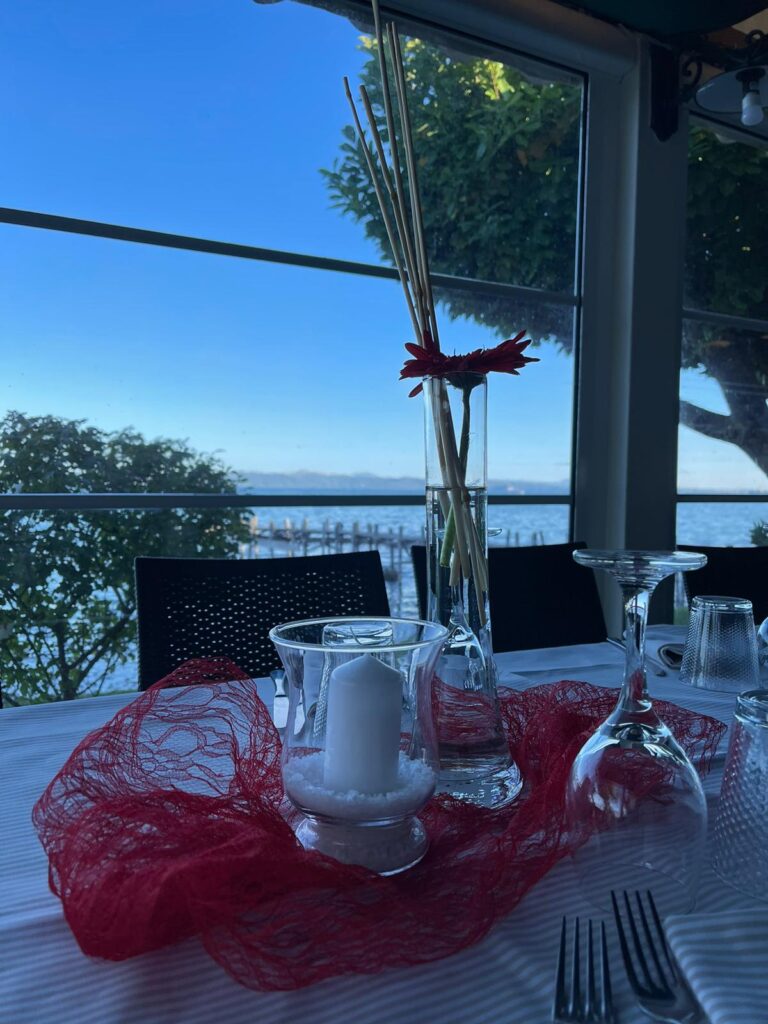Tavola apparecchiata con candela e fiore, vista lago.