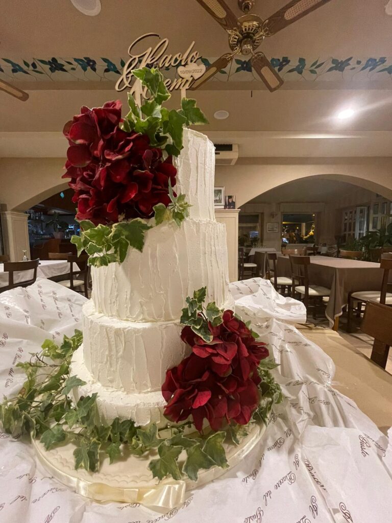 Torta nuziale bianca con fiori rossi e foglie verdi.