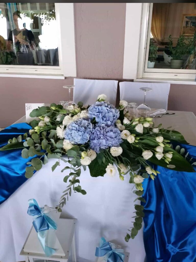 Composizione floreale blu e bianca su tavolo decorato.