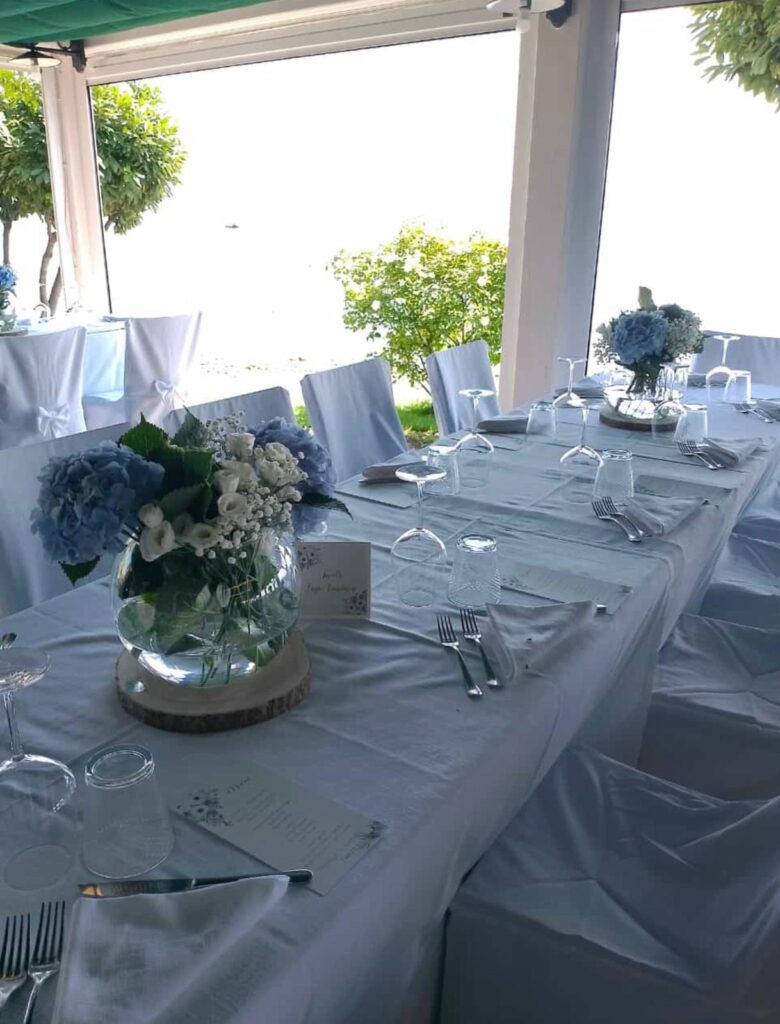Tavola apparecchiata con tovaglia bianca e fiori blu.