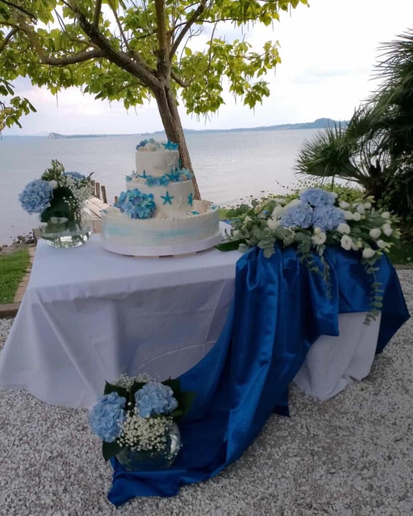 Tavolo con torta nuziale e decorazioni floreali blu.