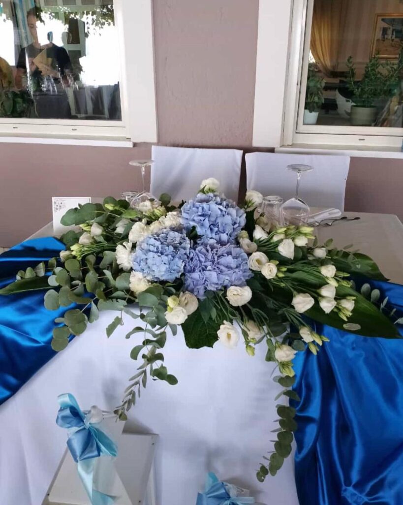 Composizione floreale blu e bianca su tavolo decorato.