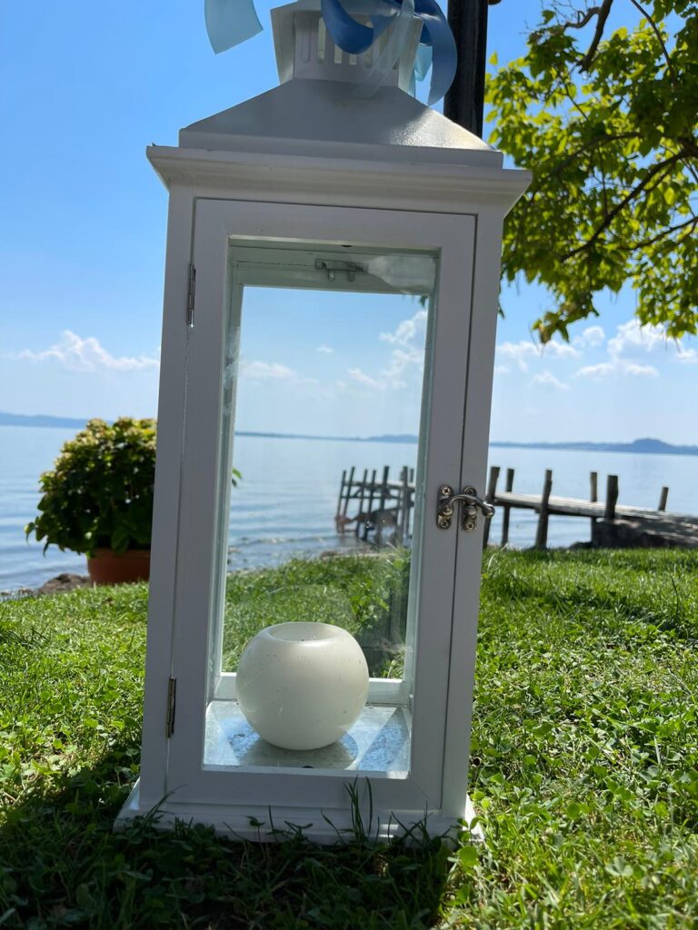 Lanterna bianca con candela su prato vicino al lago.