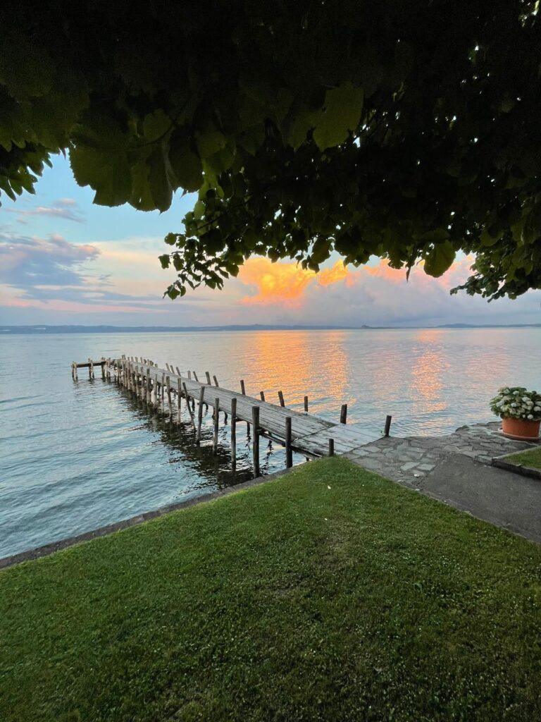 Tramonto su lago con molo e prato verde.