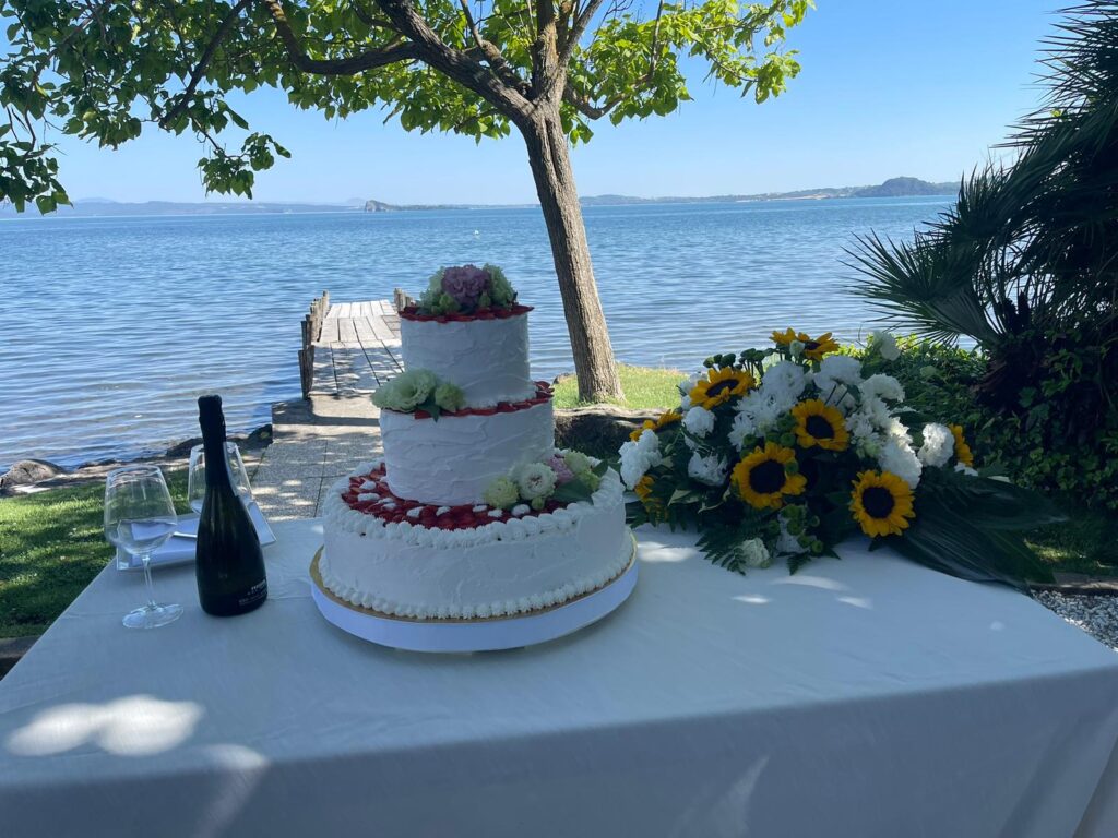 Torta nuziale e fiori su tavolo vicino al lago.