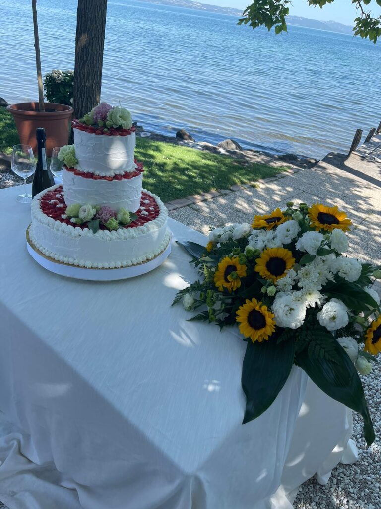 Torta nuziale e fiori su tavolo vicino al lago.