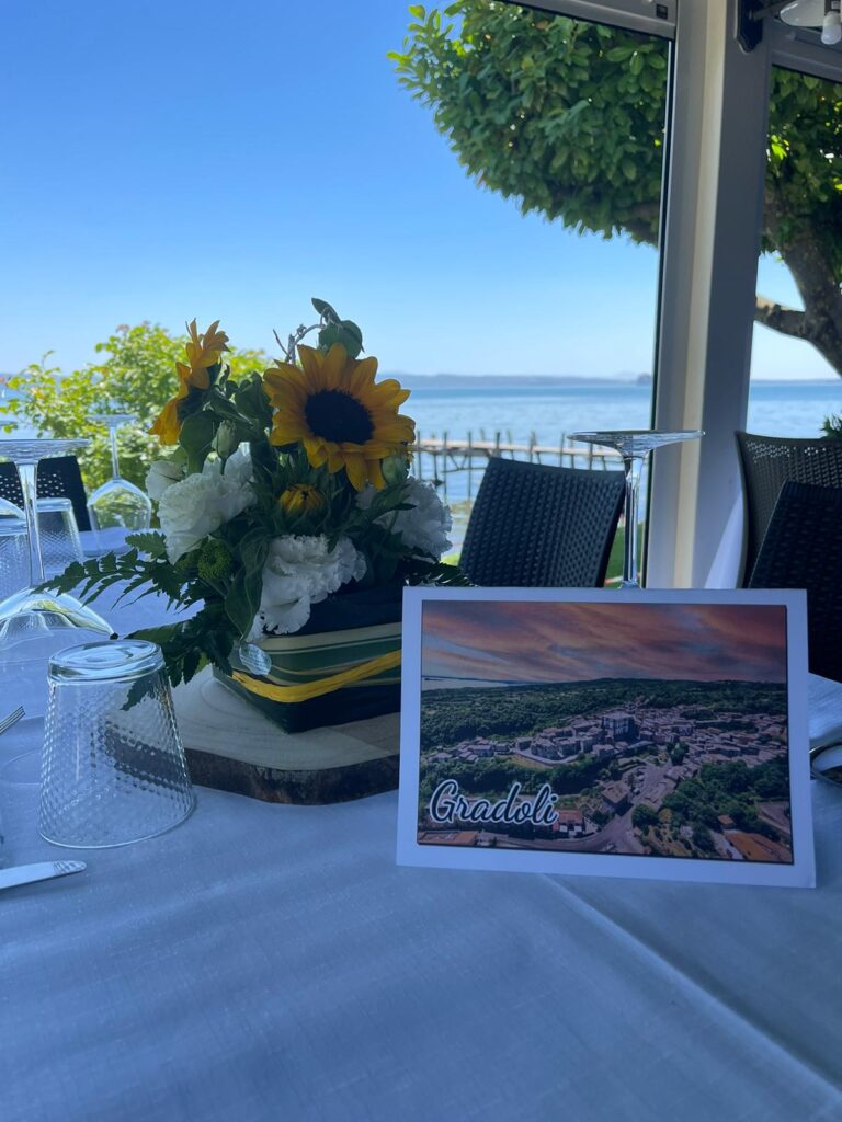 Tavolo apparecchiato con fiori e cartolina, vista lago.