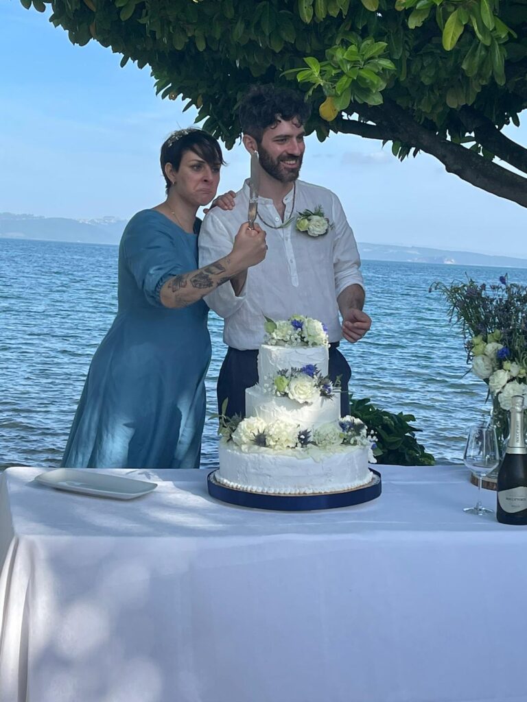 Coppia taglia torta nuziale davanti al mare.