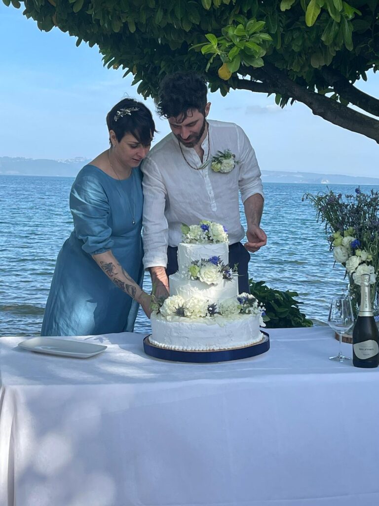 Coppia taglia torta nuziale vicino al mare.