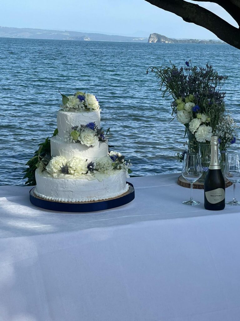 Torta nuziale a tre piani con fiori, vista mare.