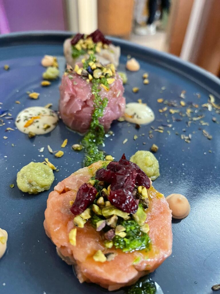 Tre tartare di pesce con pistacchi e salse su piatto.
