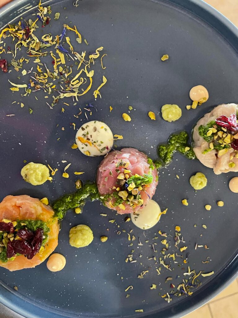Tre tartare di pesce con salse e decorazioni floreali.