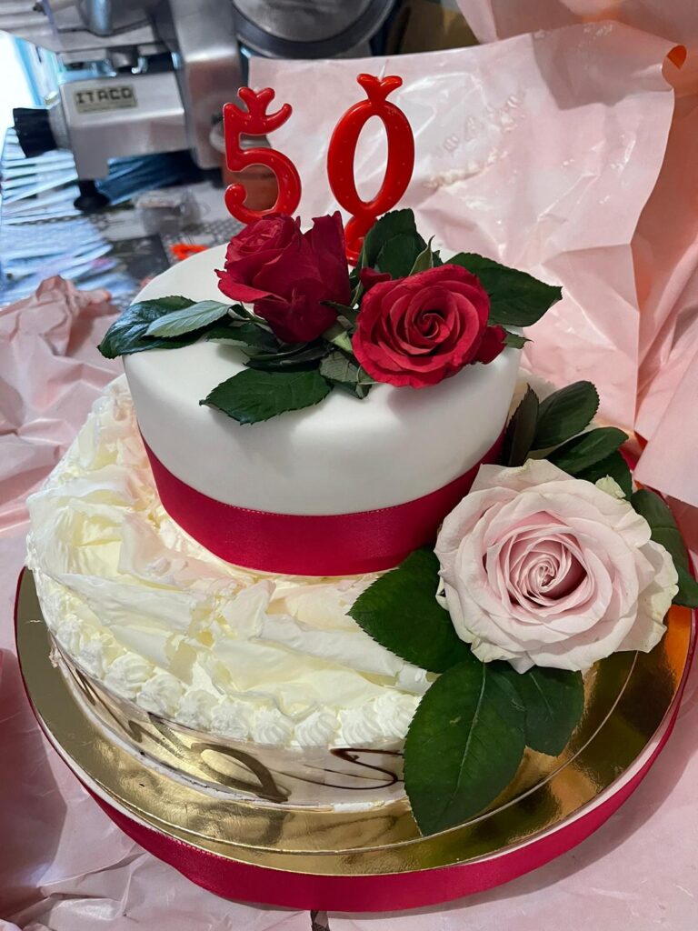 Torta con decorazioni floreali e numero 50 rosso.