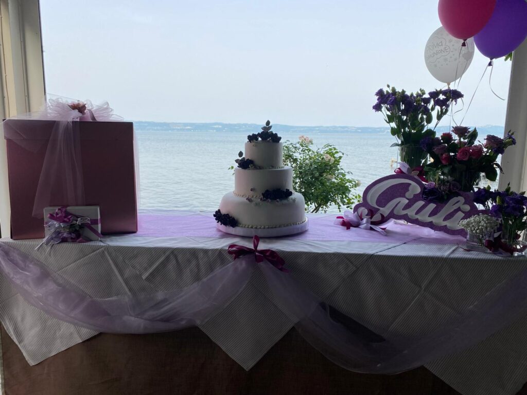 Tavolo decorato con torta, fiori e regali vista lago.