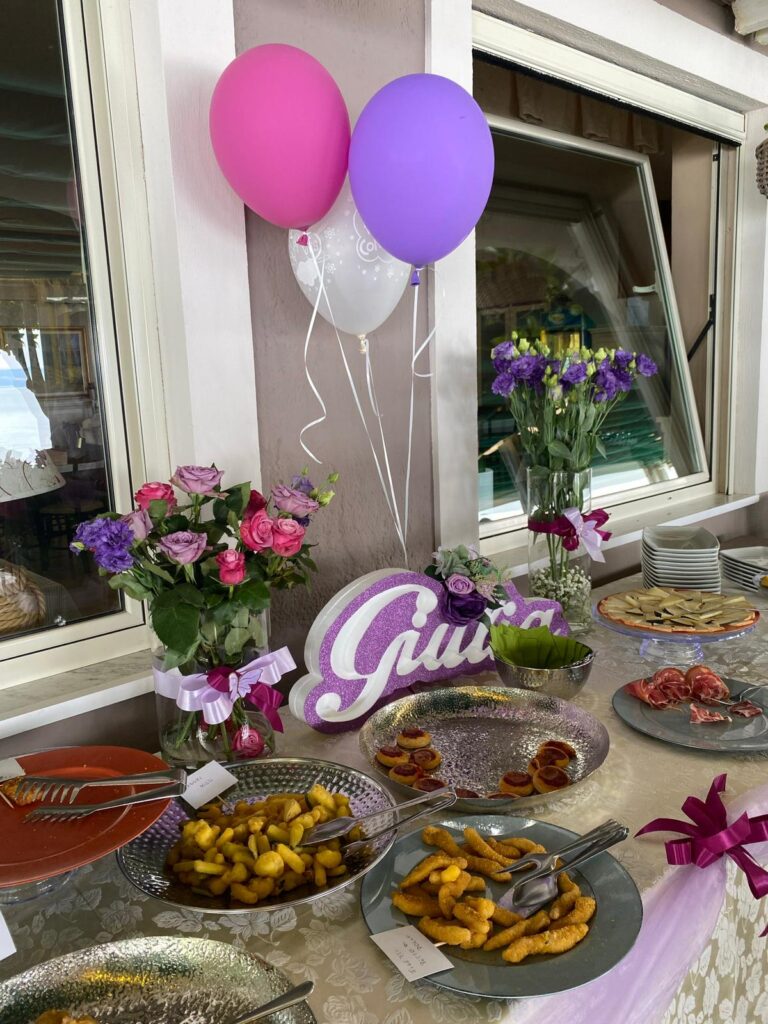 Buffet con piatti vari, fiori e palloncini colorati.