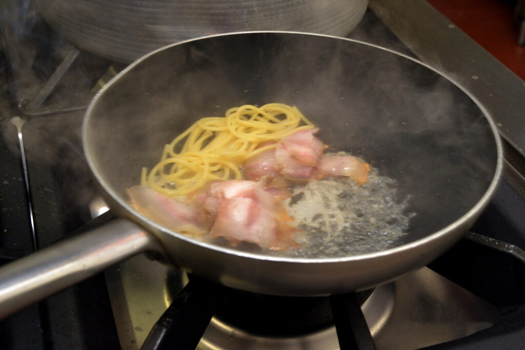 Spaghetti e pancetta in padella fumante.