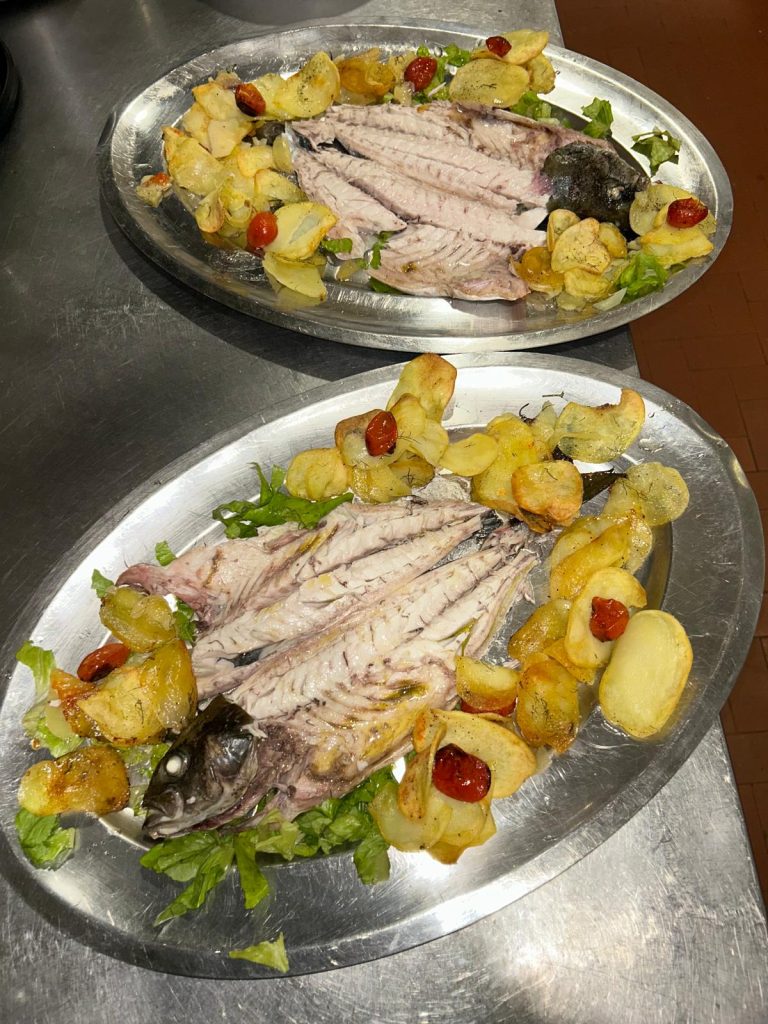 Due piatti di pesce con patate e pomodorini.
