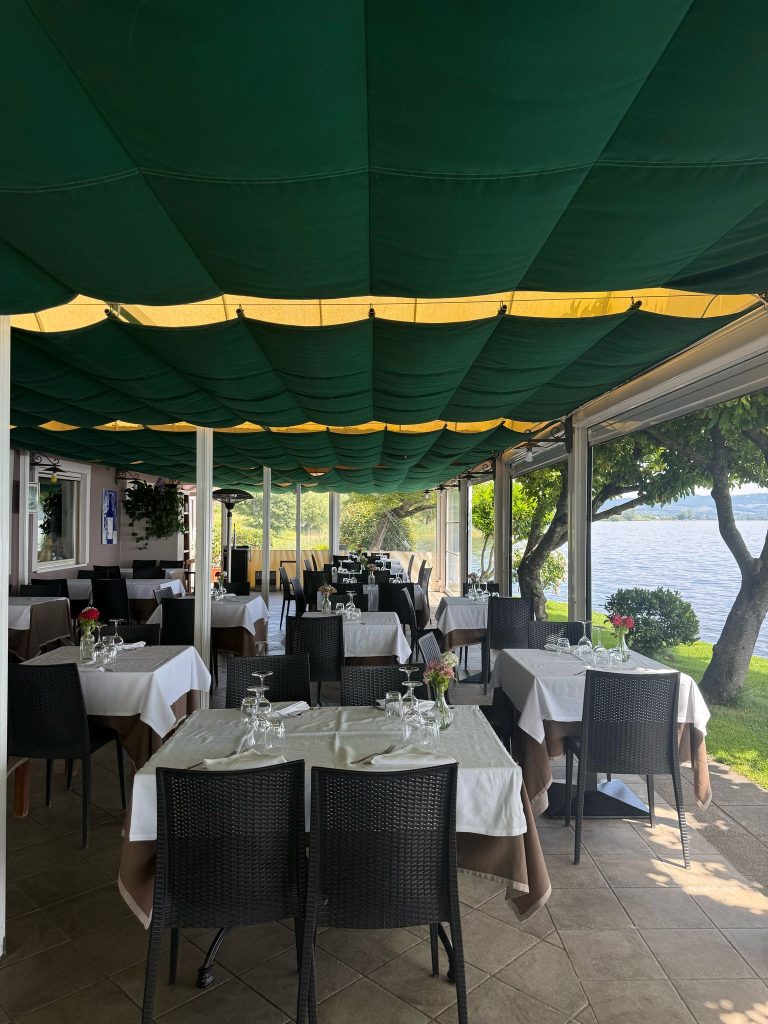 Ristorante all'aperto con tavoli apparecchiati e vista sul lago.