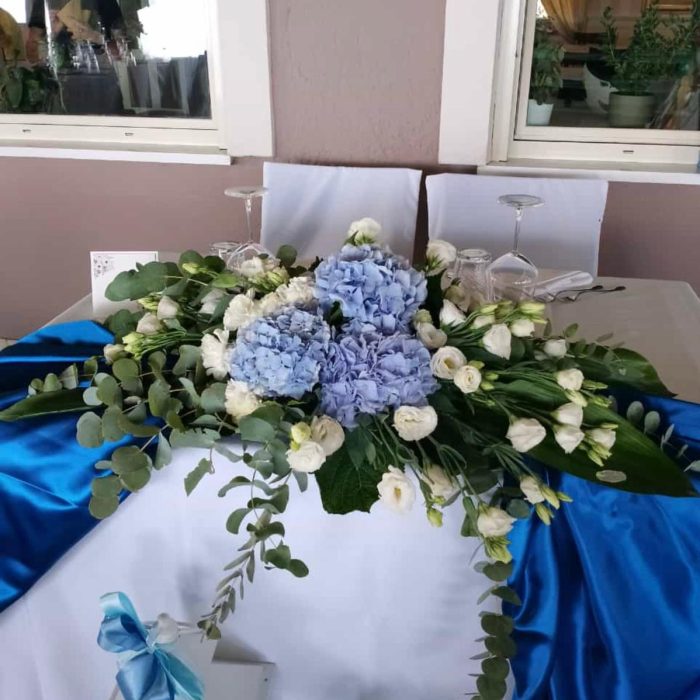 Composizione floreale blu e bianca su tavolo decorato.