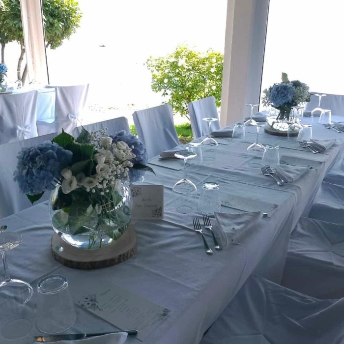 Tavola apparecchiata con tovaglia bianca e fiori blu.