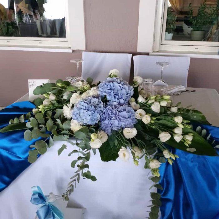 Composizione floreale blu e bianca su tavolo decorato.