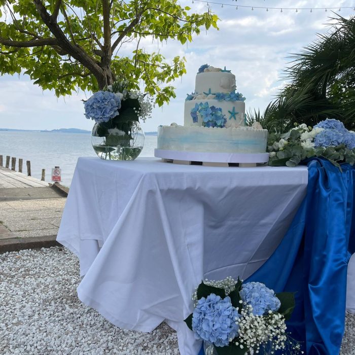 Tavolo con torta nuziale e decorazioni floreali blu.