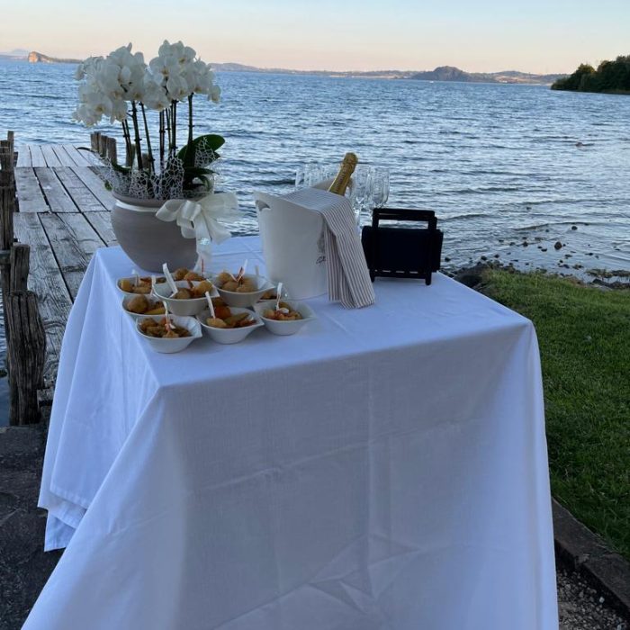 Tavolo apparecchiato con cibo e champagne vicino al lago.