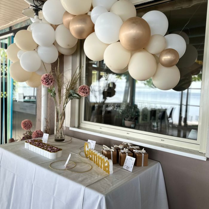 Tavolo decorato con palloncini bianchi e dorati.