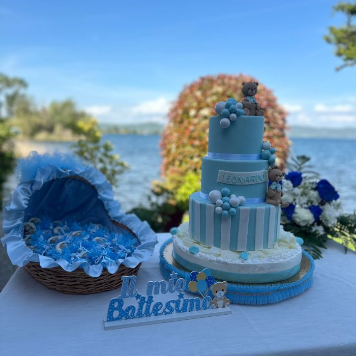 Torta battesimo blu con decorazioni orsetto, lago sullo sfondo.