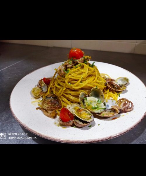 Spaghetti mit Muscheln und Kirschtomaten auf einem weißen Teller.